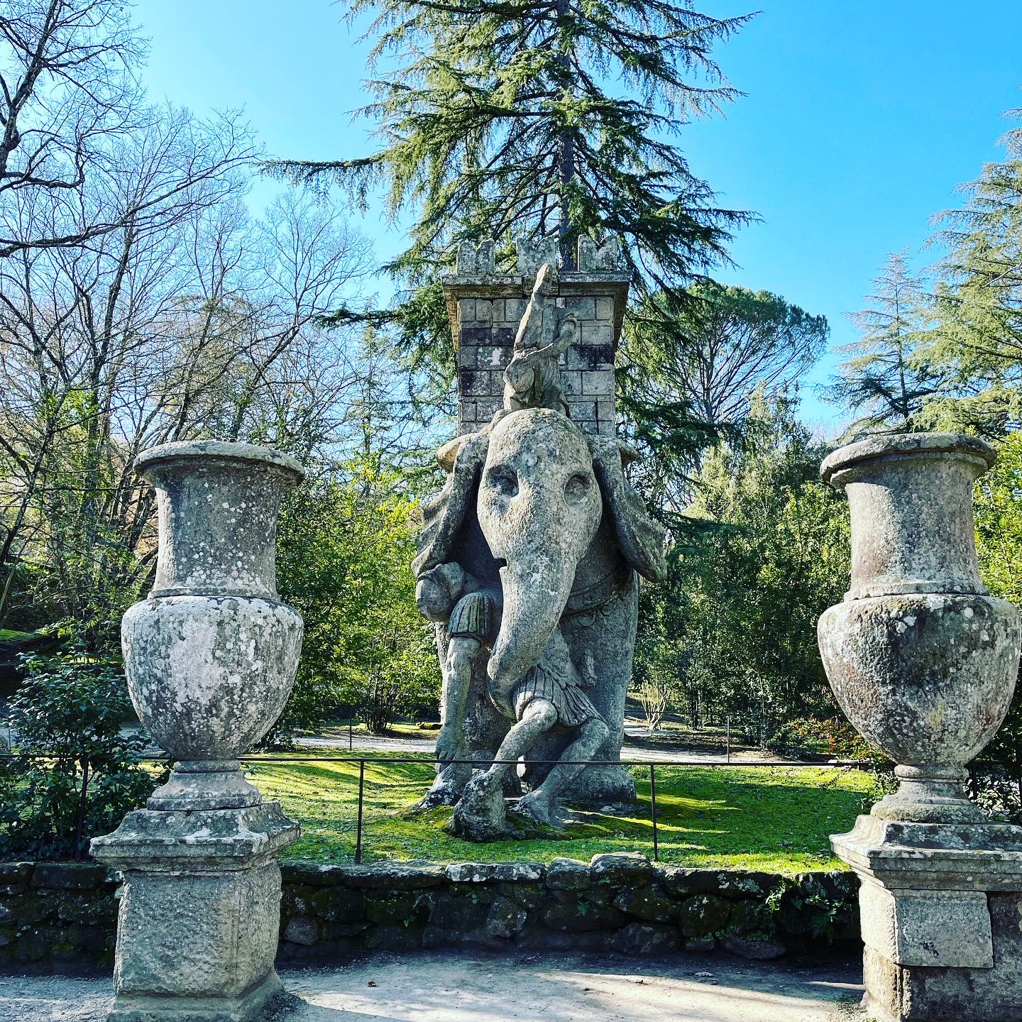 Image of sculpture from Sacro Bosco, two large sculpted vases frame an elephant, who is cradlinga soldier with its trunk.